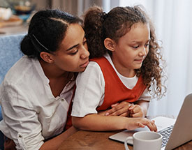 Mom looks over daughter's shoulder while she uses a laptop