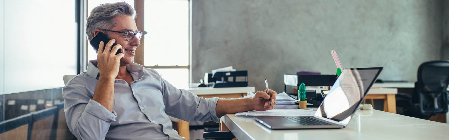 A man sitting in front of a laptop on the phone.