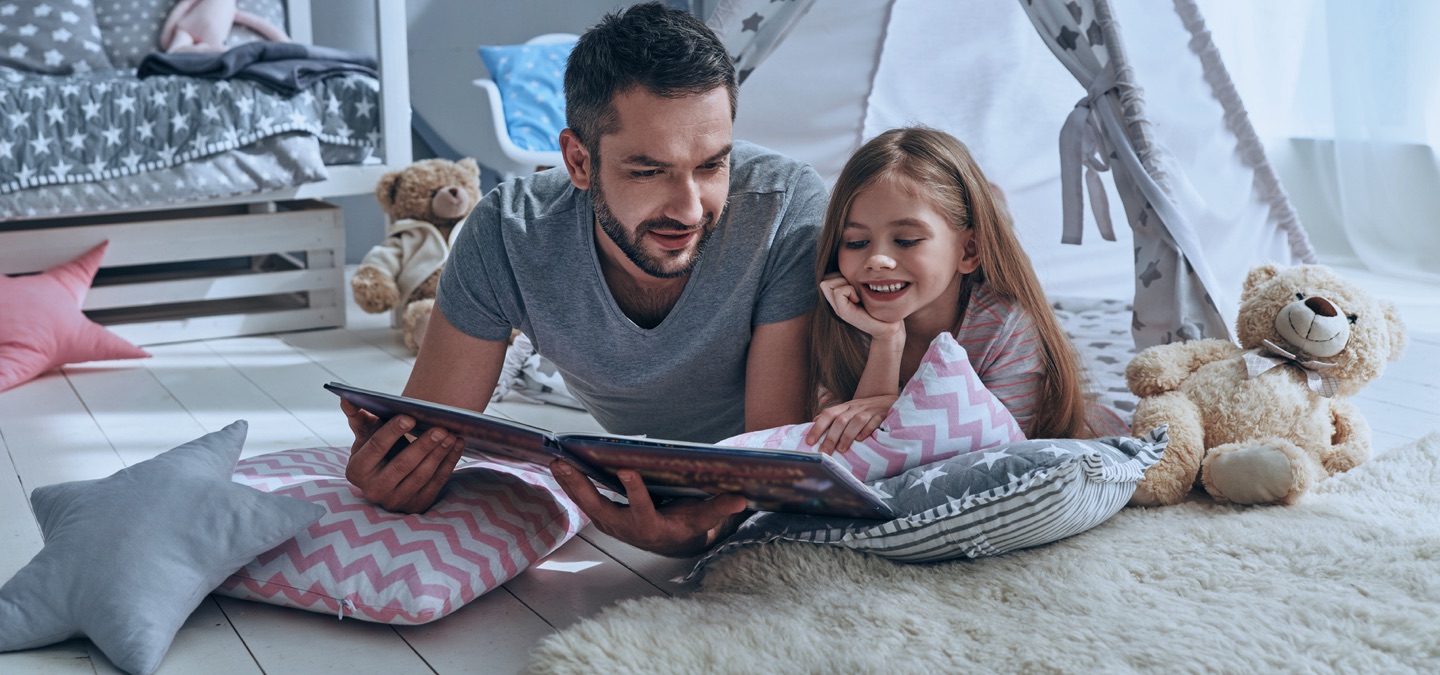 A dad and his young child reading a book together.