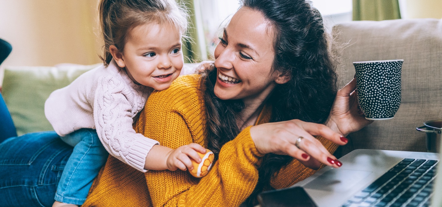 A mother and her young child playing together on a couch.