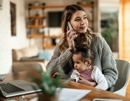 A young mother on the phone with her child in her lap.