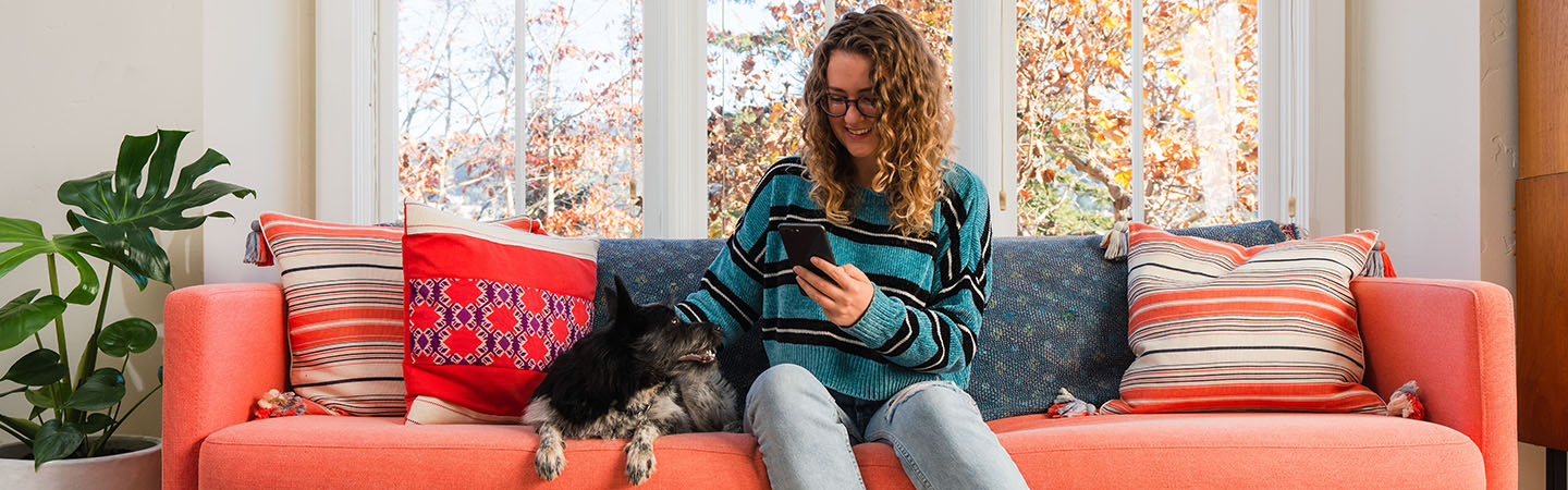 Girl sitting on a couch looking at her smartphone while sitting next to a dog