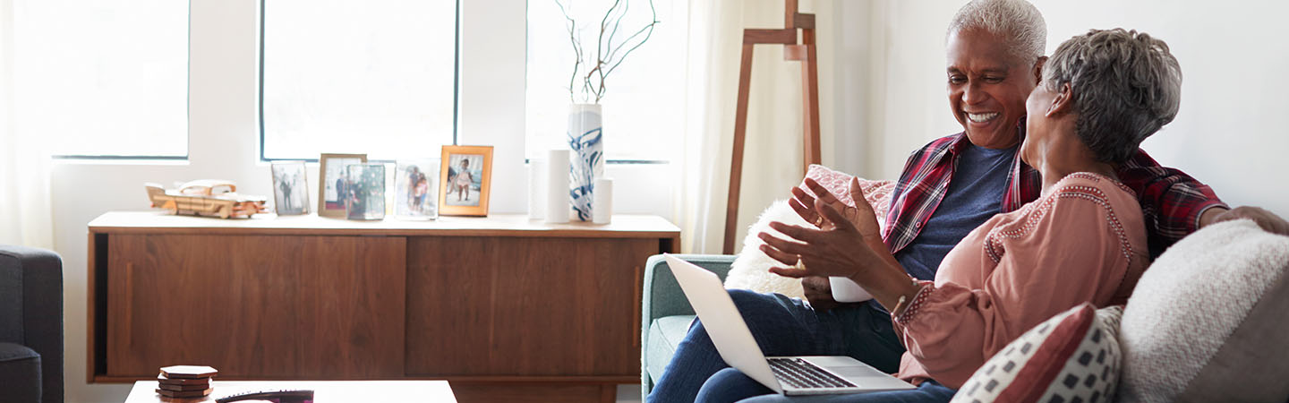 An older couple sitting on a couch and using a laptop